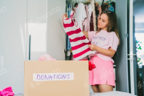 Preview: A cardboard box of selected clothes for donating to a Charity shop standing on the bed. Decluttering