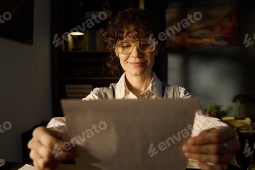 Preview: Portrait of Young Adult Caucasian Woman Smiling While Reading Document Indoors