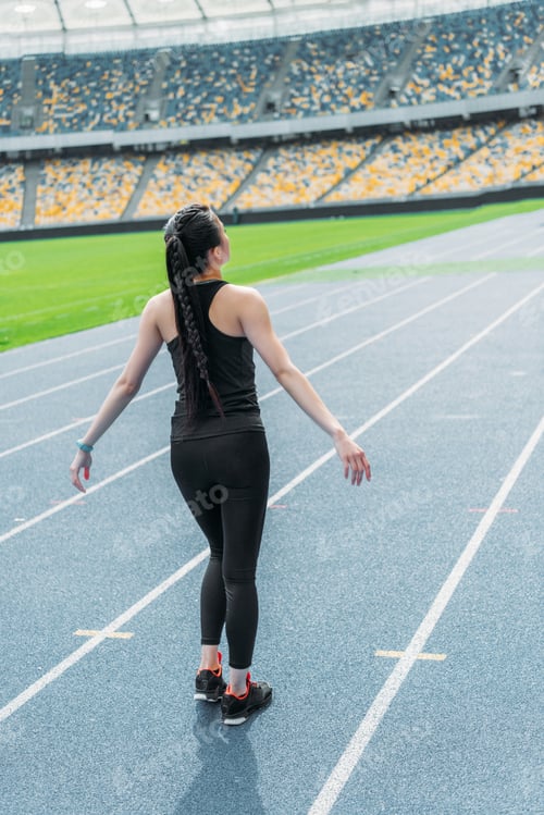 Preview: Back view of young fitness woman in sportswear standing on running track stadium