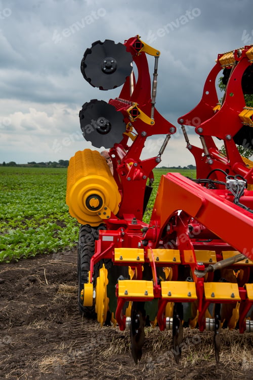 Preview: red and yellow harrow-cultivator standing folded for transportation near a field
