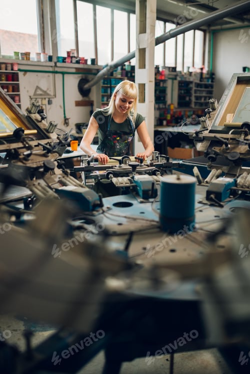 Preview: Young graphic worker is screen printing on carousel printing machine.
