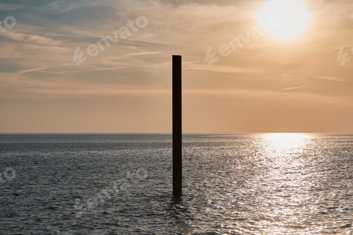 Preview: Large rusty steel construction pillar in blue sea with calm waves at sunset, abandoned building part