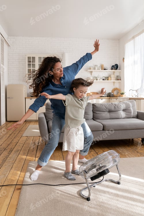 Preview: Overjoyed mom and small kid have fun at home play with wind from ventilator cheering and bonding