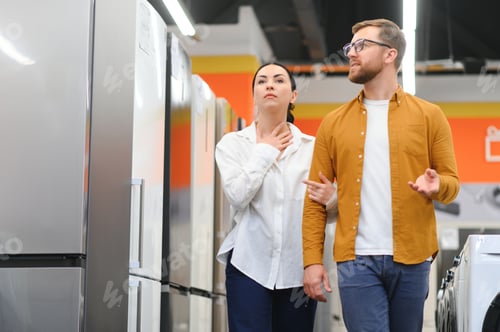 Preview: Young couple, satisfied customers choosing fridge in appliances store