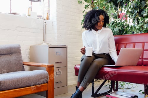 Preview: Woman in office sitting on sofa using laptop