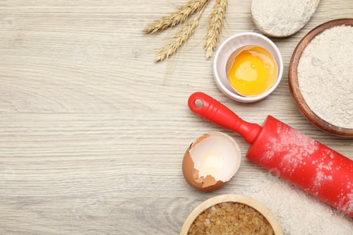 Preview: Rolling pin and different ingredients on light wooden table, flat lay. Space for text