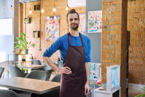 Preview: Young man worker, owner in apron looking at camera in restaurant, coffee shop