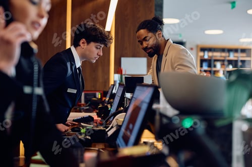 Preview: Smiling black man checking in at hotel reception desk.