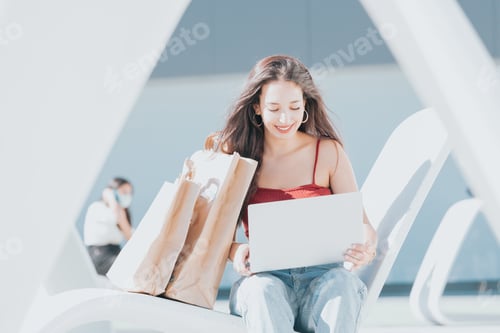 Preview: Portrait of a young woman shopper checking his laptop surrounded by bags happy