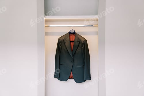 Preview: Groom black jacket hangs on a hanger in a white sliding wardrobe in the room