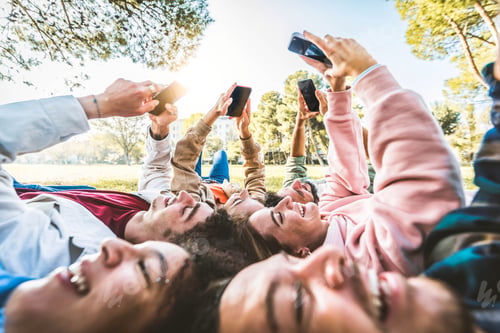 Preview: Group of young people using smart mobile phone device lying on the grass