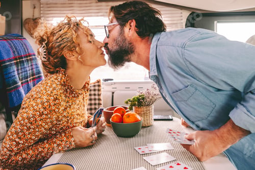 Preview: Couple enjoy leisure time playing cards and kissing with love inside a camper van. Travel HOL