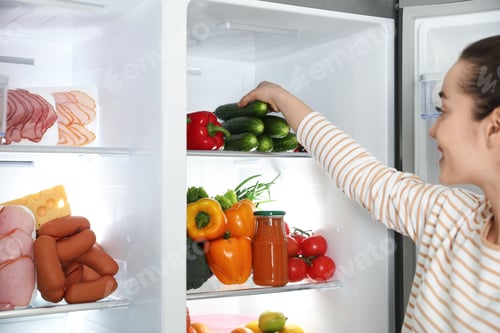 Preview: Young woman taking cucumber out of refrigerator, closeup