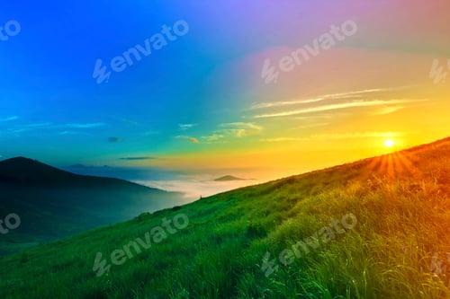 Preview: Sunrise over hills in mountains with green grass and blue sky wi