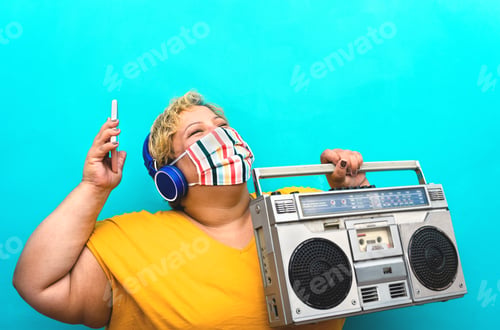 Preview: Happy plus size woman listening music with mobile smartphone and headphones while holding boombox