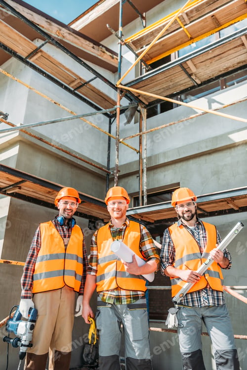 Preview: group of smiling equipped builders looking at camera at construction site