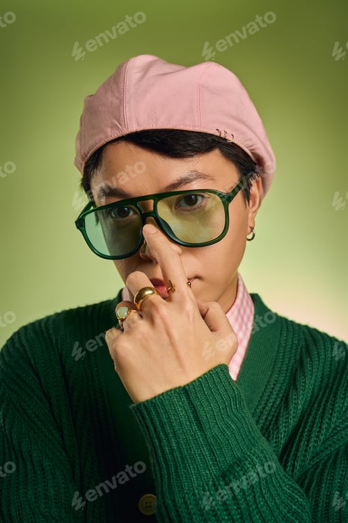 Preview: Stylish asian man poses confidently in vibrant green studio wearing pink checked shirt