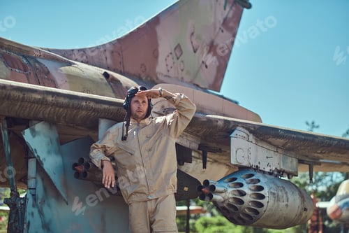 Preview: Mechanic in uniform and flying helmet standing near an old war fighter-interceptor