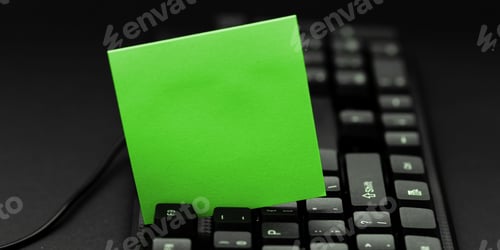 Preview: Closeup of a green sticky note positioned between two black keys on a keyboard, with copy space