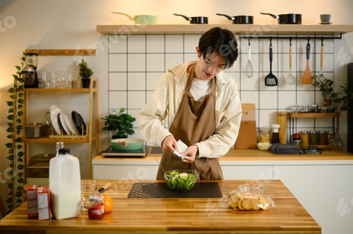 Preview: Young man pours dressing onto a bowl of fresh vegetable salad