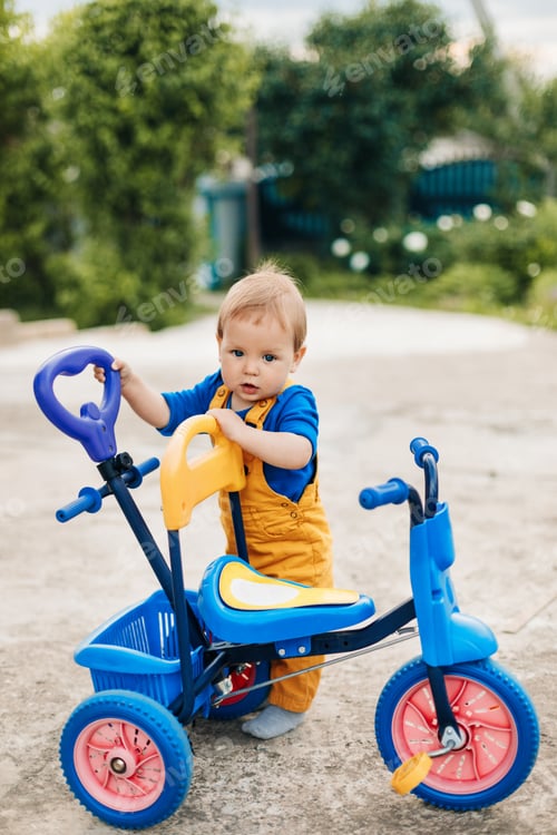 Preview: A small boy stands next to a child's tricycle. First bike, new skills