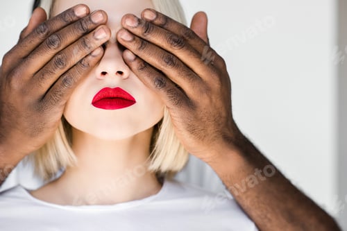 Preview: cropped image of african american boyfriend closing eyes of blonde girlfriend