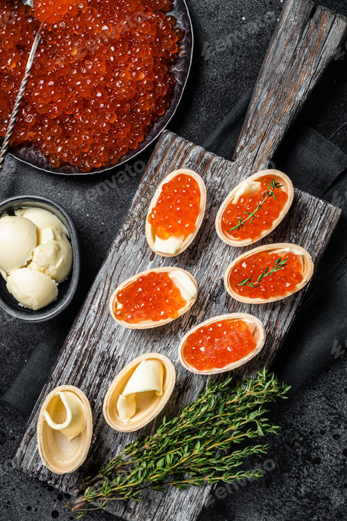 Preview: Tartlets with Red caviar, butter and thyme on wooden board. Black background. Top view