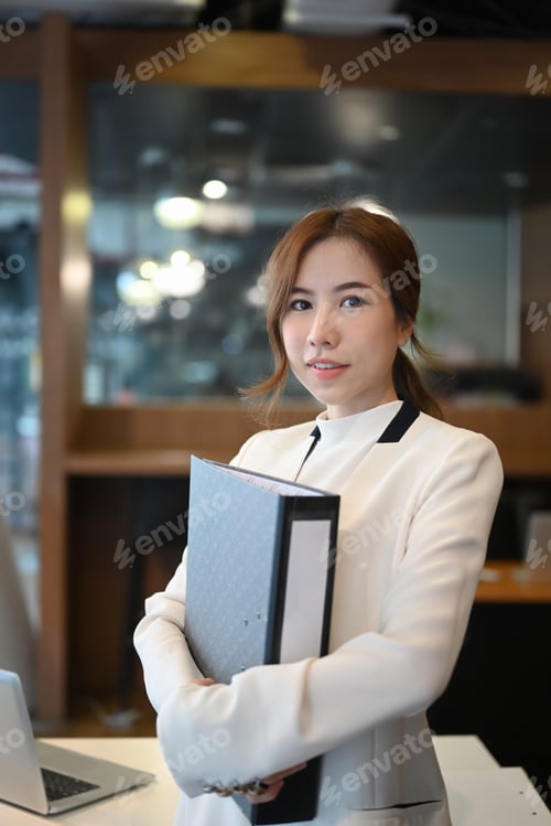 Preview: Portrait of confident businesswoman holding business file folder and standing in modern office.