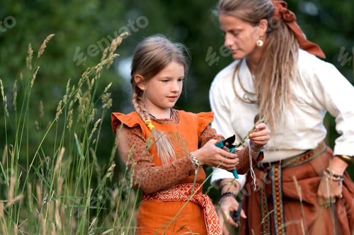 Preview: Midsummer celebration countryside- mom and girl wearing national costumes collect medicinal plants