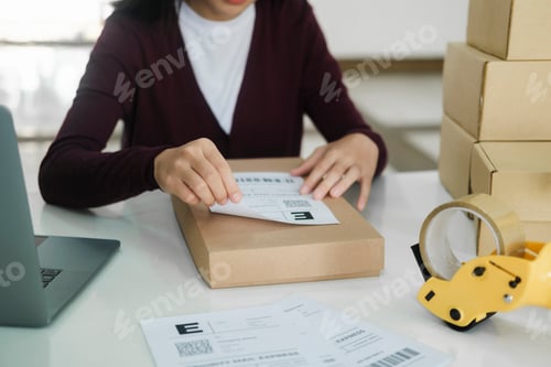 Preview: Young business owner putting shipping label on parcel.