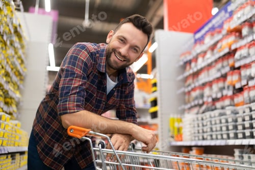 Preview: happy customer with a smile on his face next to a shopping basket in a hardware store between rows