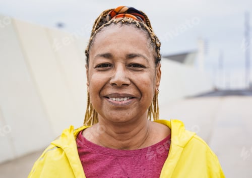 Preview: Happy senior african woman smiling on camera after sprot workout in the city during rainy day