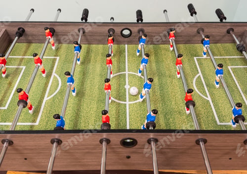 Preview: Classic Foosball Table Game With Players in Red and Blue Jerseys During Daytime Indoor Match. Close