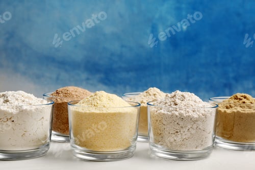 Preview: Bowls with different types of flour on table against color background. Space for text