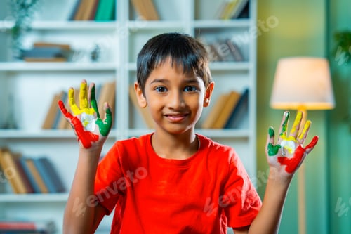 Preview: Playful Indian asian boy with painted palms, smiling cheerfully during a fun art activity at home