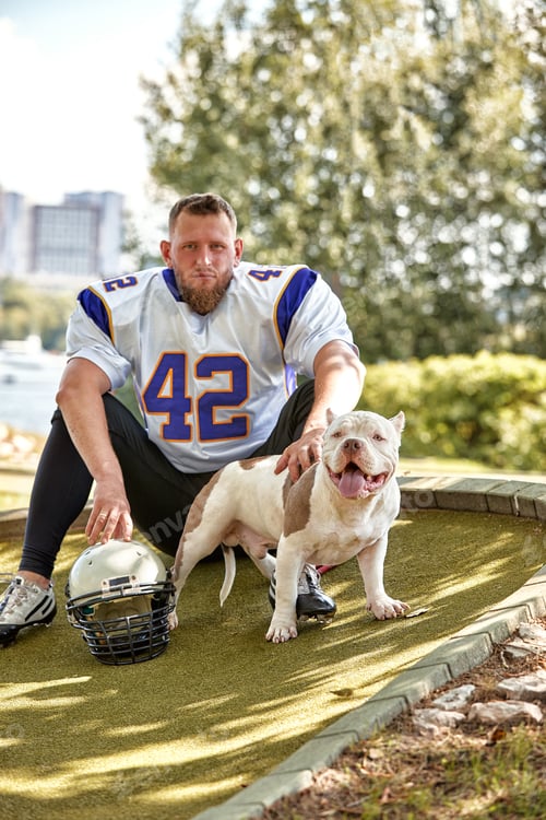 Preview: American football player with a dog posing on camera in a park. Copy space, sports banner. Concept