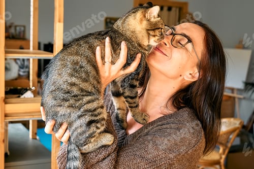 Preview: Middle-aged woman hugging cute tabby cat in indoor scene. Human-animal relationships. Funny home pet