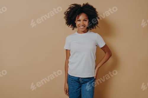 Preview: Cheerful african female in white tshirt and jeans expressing positive emotions, posing in studio