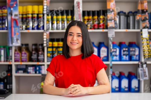 Preview: Woman employee in red shirt standing behind a counter in an auto parts retail store