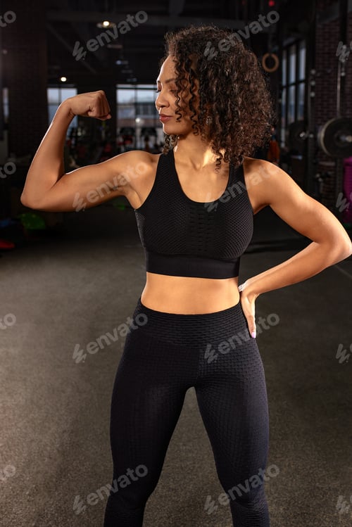 Preview: A young African American woman shows her muscles on her arms. Portrait photo of an athletic woman