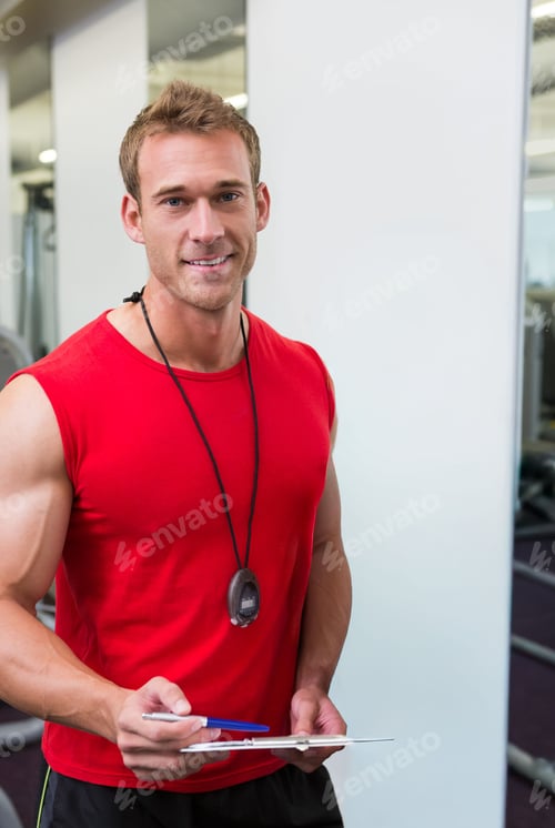 Preview: Male trainer standing in gym wearing red tank top black shorts holding clipboard stopwatch blue pen