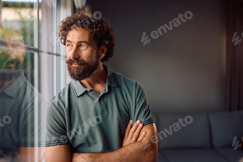 Preview: Pensive man looking through the window at home.