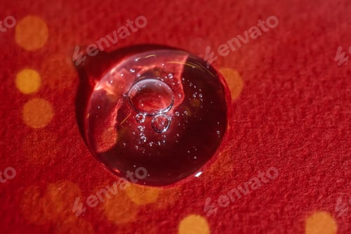 Preview: A drop of serum on a red background with bokeh.