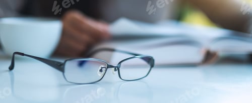Preview: Eyeglasses on Table with Person Reading Book