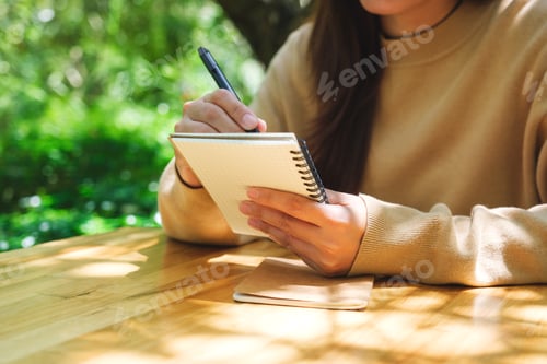 Preview: Closeup image of a woman writing on a notebook in the outdoors
