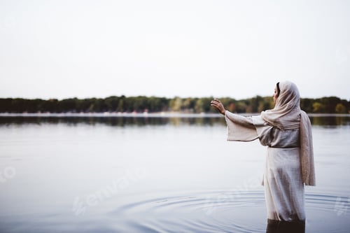 Preview: Female wearing a biblical robe and standing in the water with her hand up