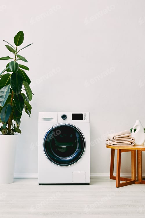 Preview: green plant near washing machine and wooden coffee table with towels and detergent bottle in