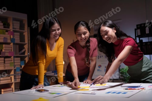 Preview: Three young businesswomen smiling and working late in the office using sticky notes