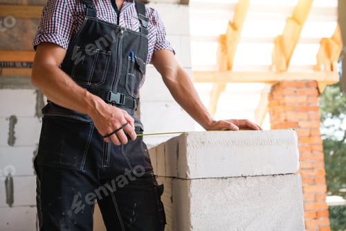 Preview: Construction worker at construction site measures the length of window opening and brick wall