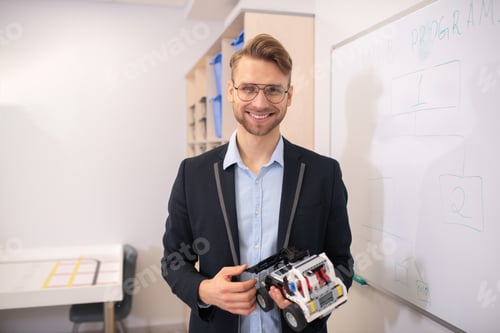 Preview: Male teacher standing at whiteboard, holding buildable car